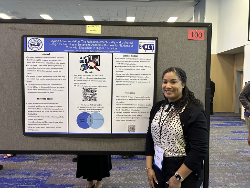 Photo of Mishon at Meeting of the Minds 2023, in front of her poster.